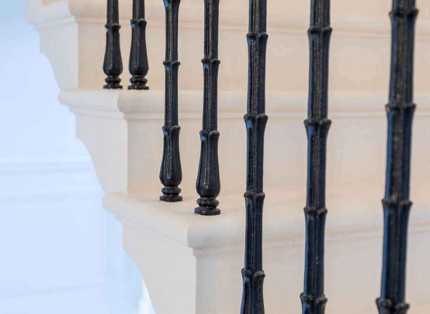 bespoke cantilevered white limestone staircase with black ornate cast iron spindles by Carvero